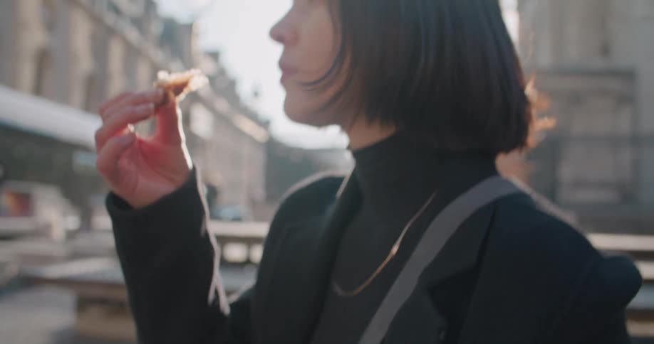 A woman sitting in middle of downtown in the city eating a croissant