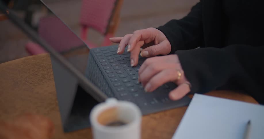 A woman types on her laptop while sitting outdoors at a cafe