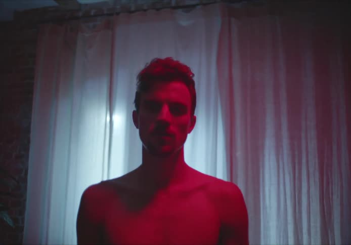 A man stands in a living room with no shirt on