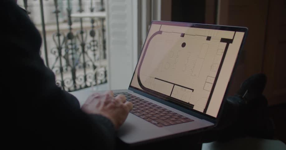 Man with black sweater works on laptop with building plan in apartment building