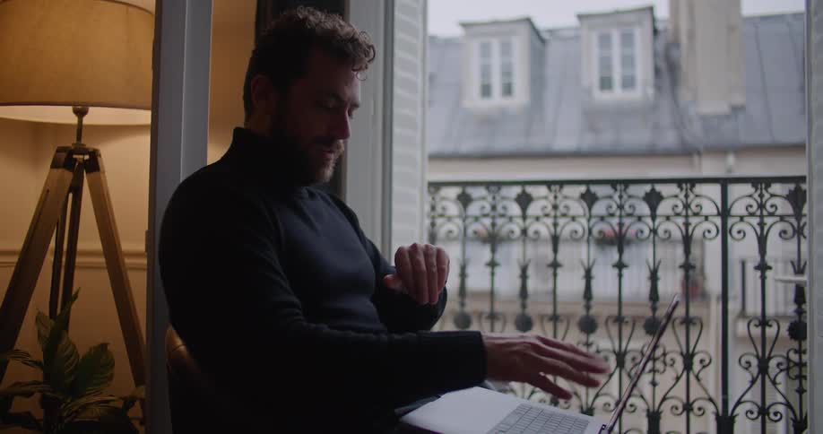 A man chats via video call on his laptop while sitting next to his balcony