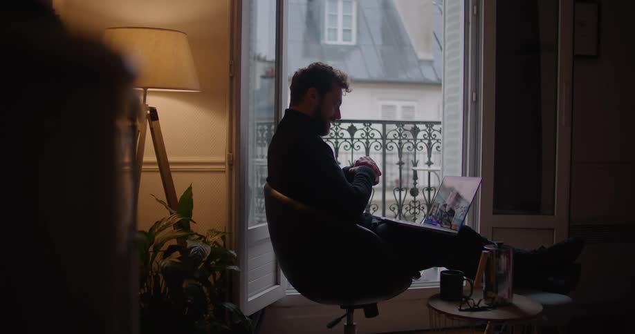 Man sits in chair with his legs up video calling on laptop