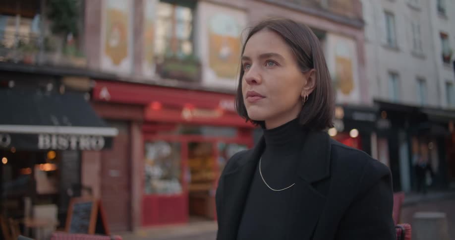A woman stands in a street and looks at the businesses around her