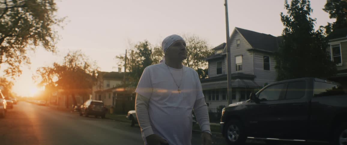 Man wearing white clothes walking down the street of a neighborhood at evening
