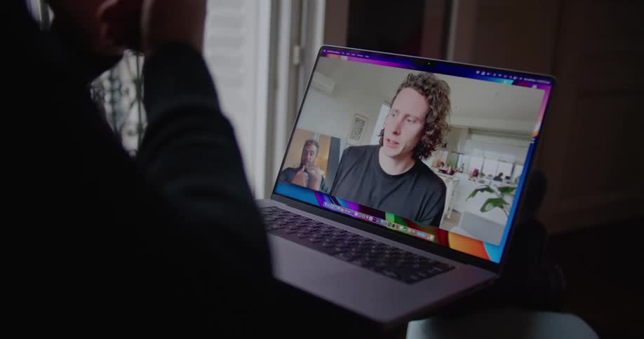 A man on a computer screen drinks coffee at home as he video chats with another man