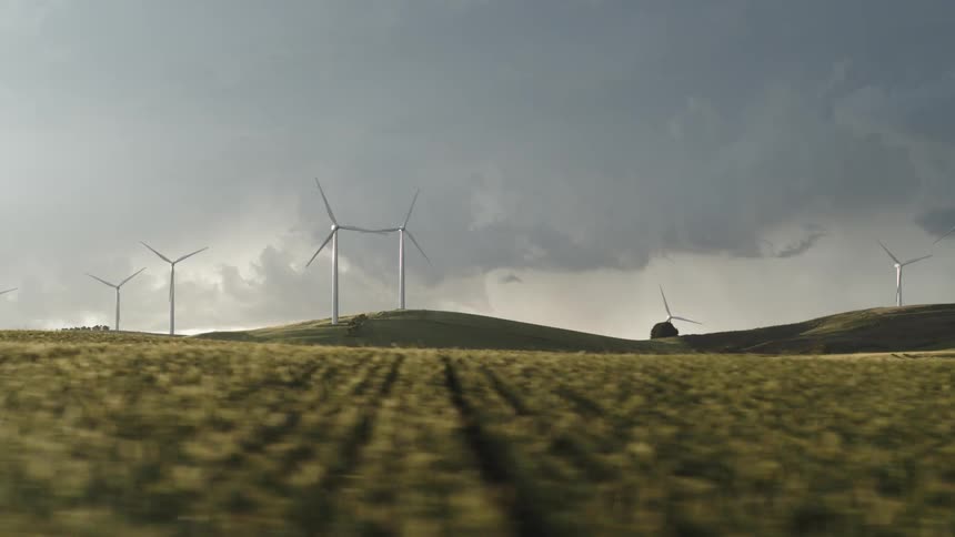 Aerial view of wind turbines spinning over the hills near the field at morning
