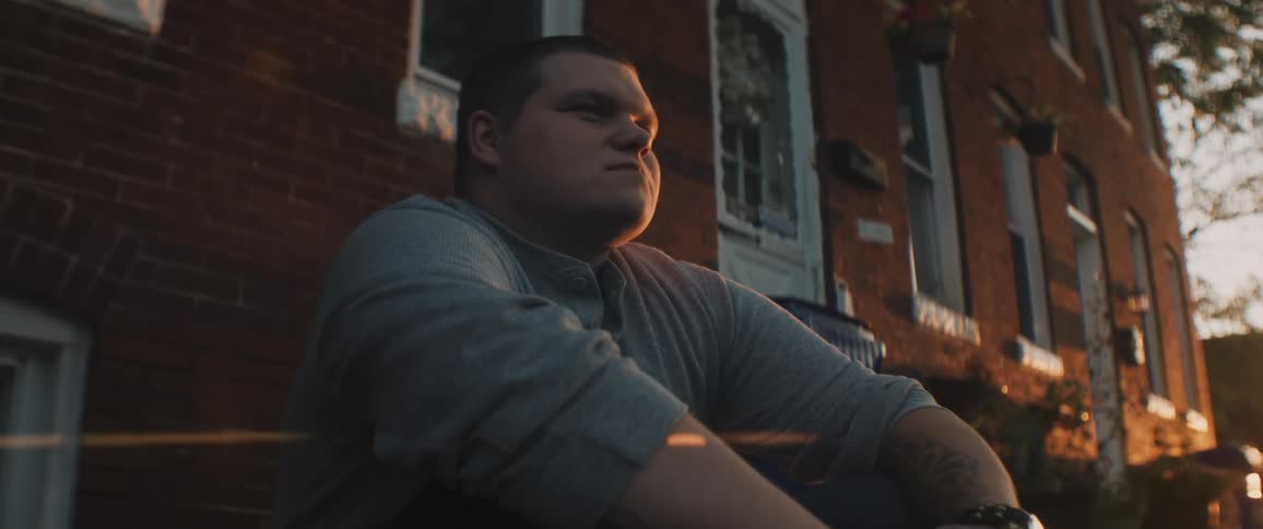 Man sitting on the stairs at the entrance of a building in a neighborhood at sunset