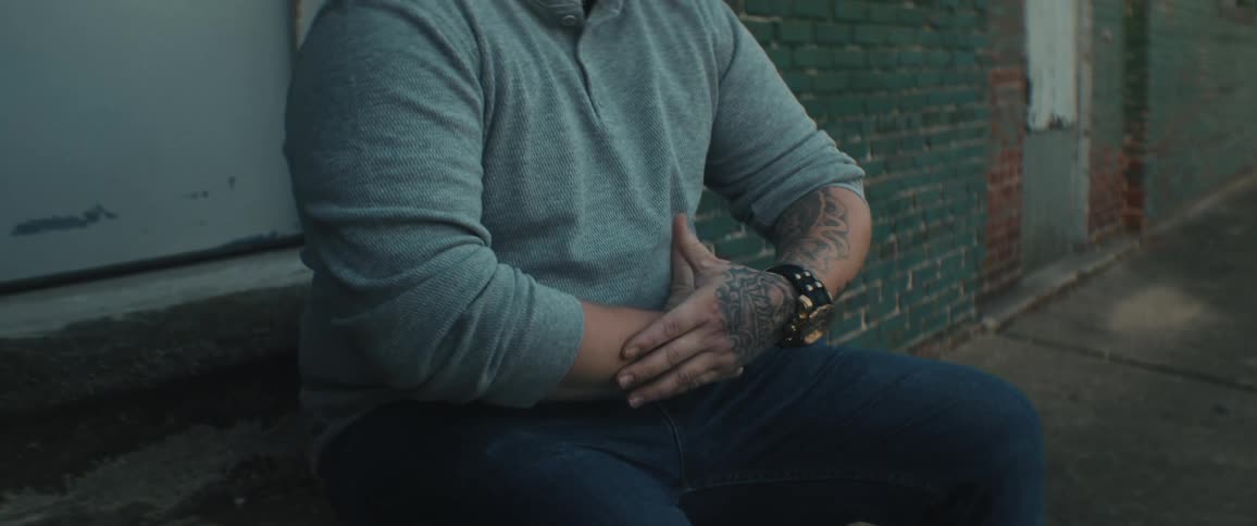 Man with tattoos on hand and arms sits on door stoop