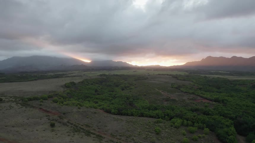 Aerial view of field with distant mountains under clouds at sunset