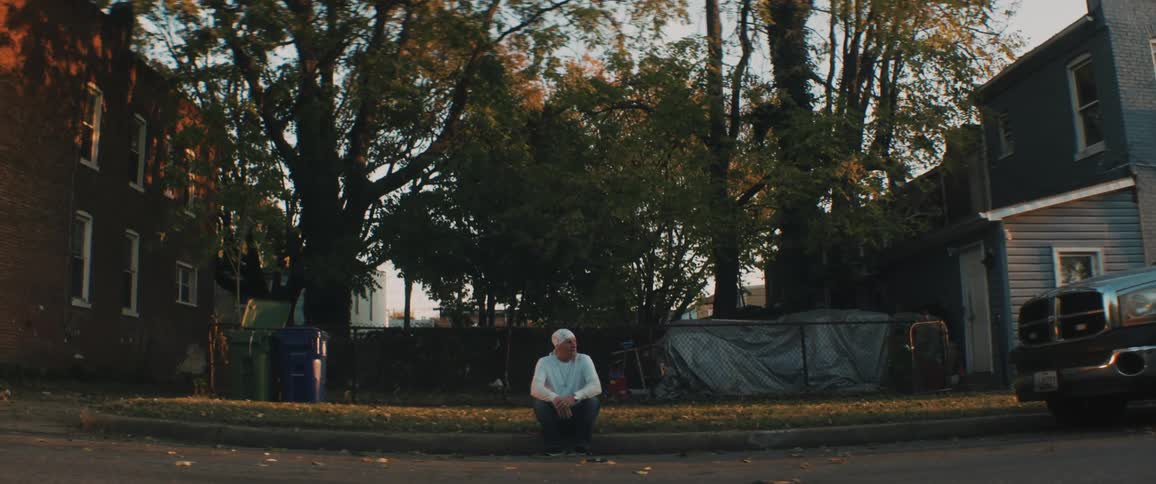 A man sits on a curb in a neighborhood