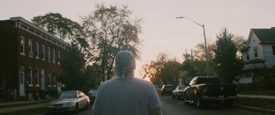 Man wearing white clothes walking down the street of a neighborhood at evening