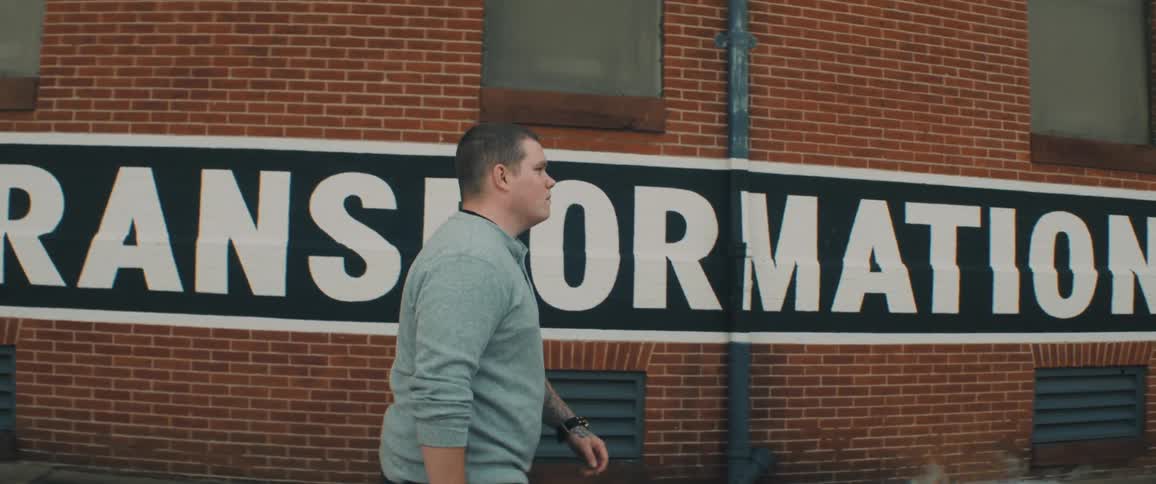 A man is walking past the building with a painted sign on the bricks