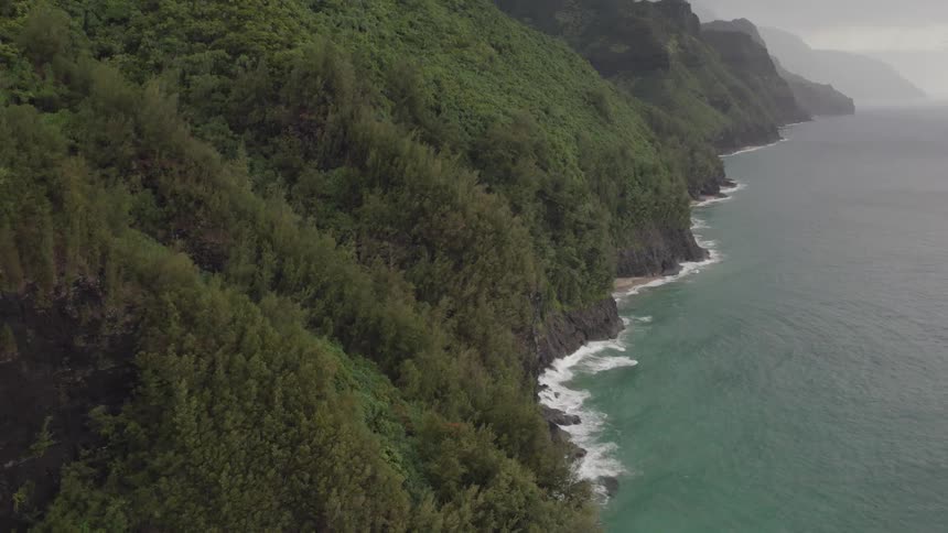 Waves crash onto the bottom of a promontory covered in trees