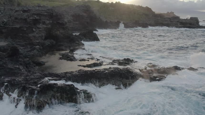 Aerial view of waves crashing on the rocks in the coast near the mountains at morning