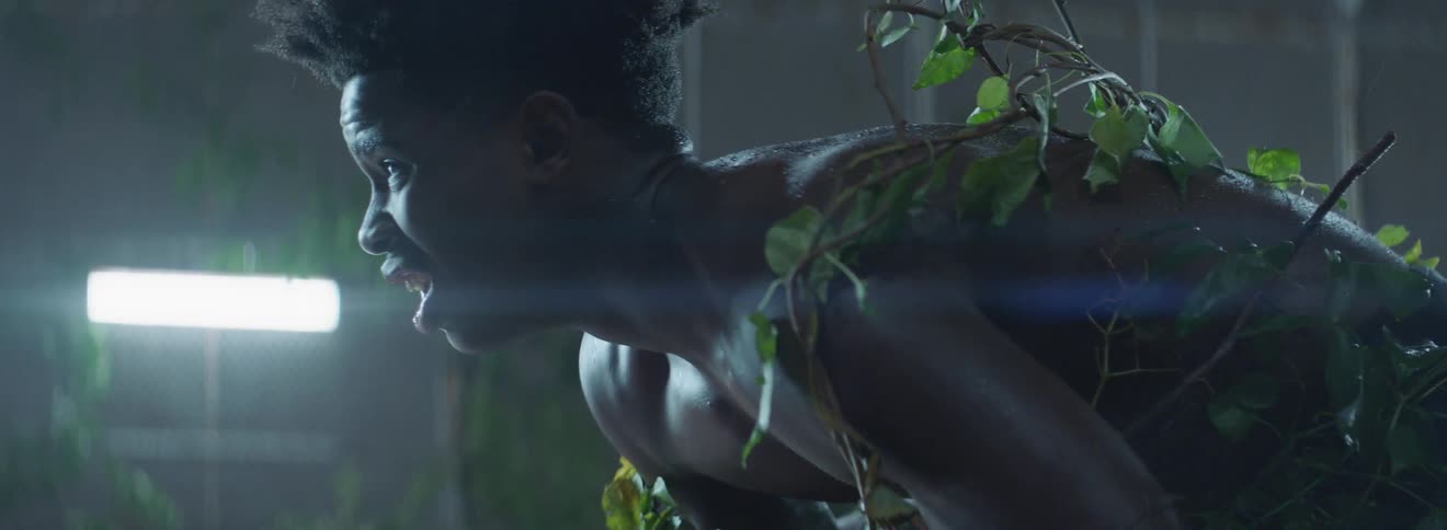 A man is wincing as he leans forward covered in vines