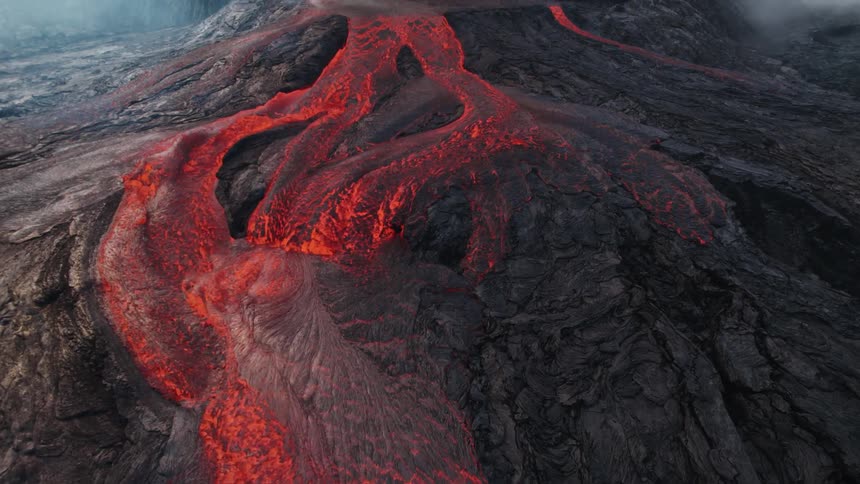 Lava runs down the side of an erupting volcano shrouded in smoke