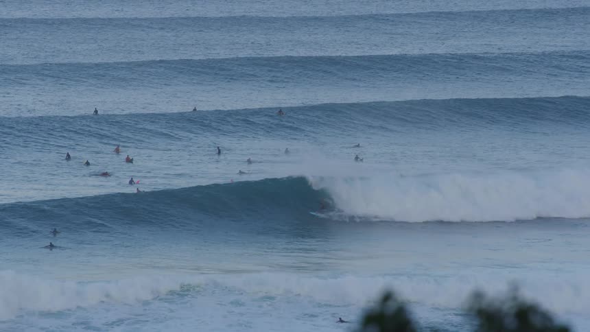 A person is surfing a large wave as other people are floating in the ocean
