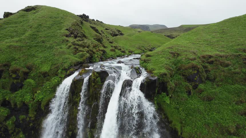 Aerial view of a waterfall flowing over the green cliffs covered in vegetation
