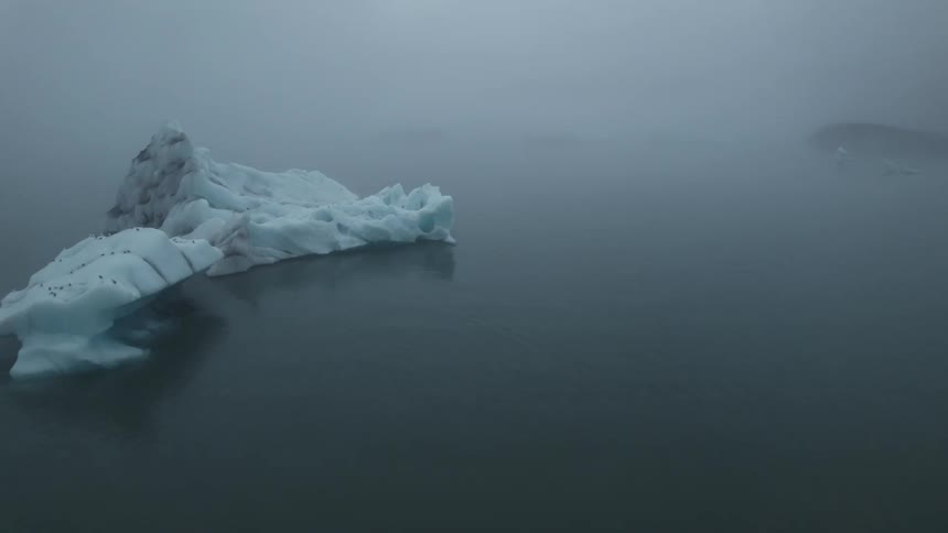 Aerial view of icebergs floating on the ocean under the thick white fog