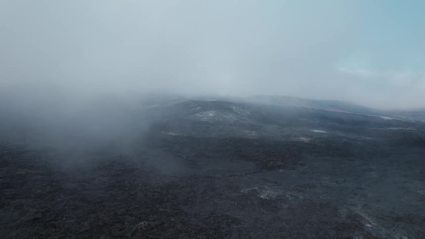Aerial view of the dark terrain of a volcanic area under the white smoke