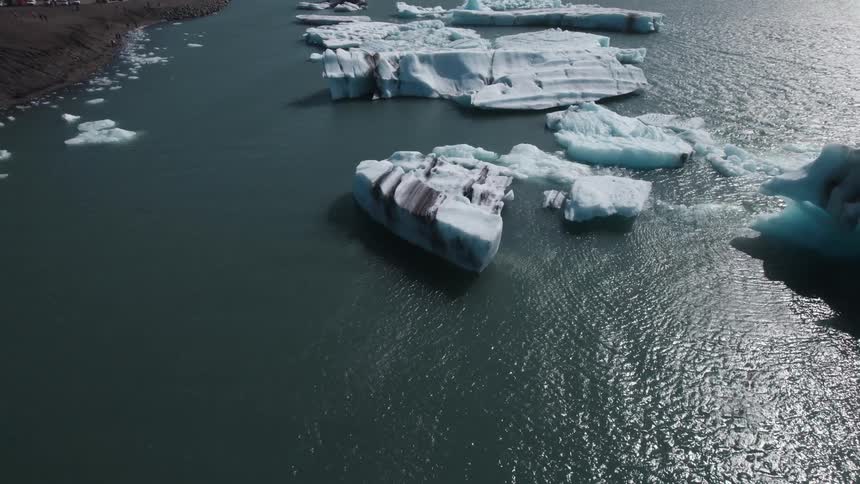 Large chunks of ice float near shore on rippling shimmering water