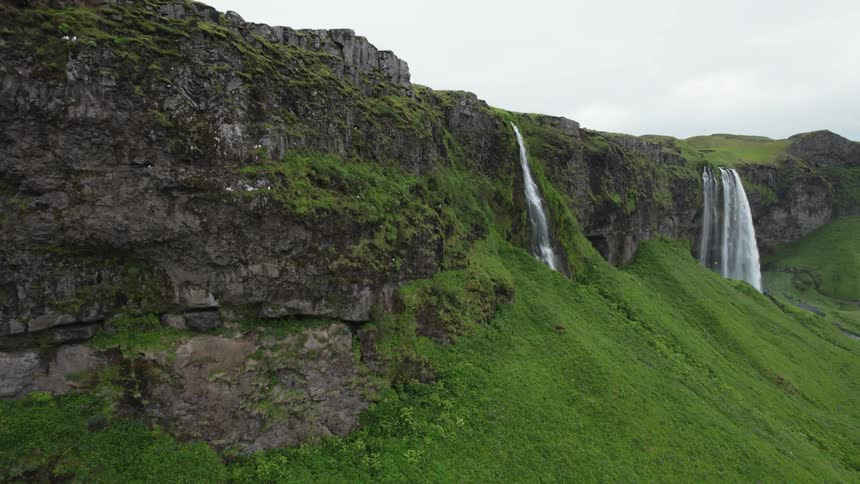 Water flows off the green and rocky cliffs splashing below as birds fly by