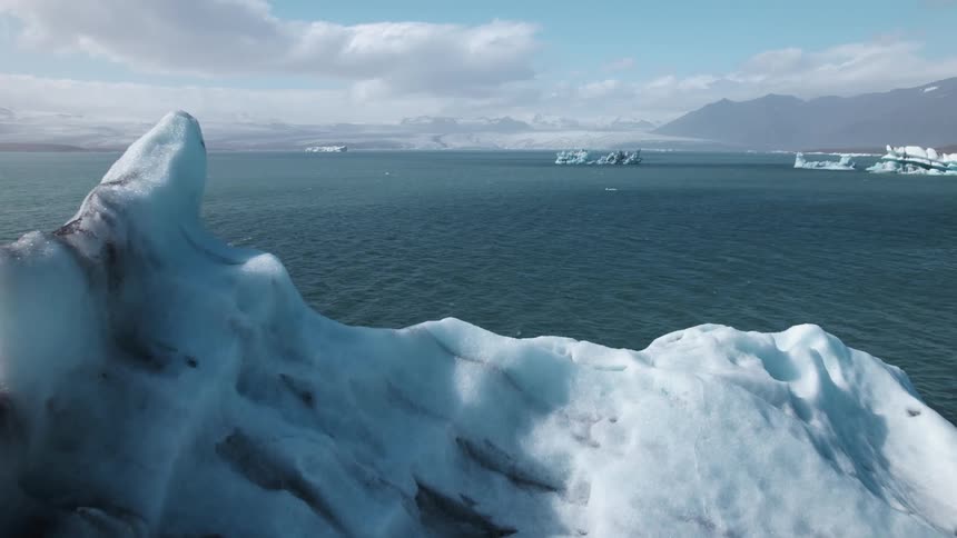 Aerial view of icebergs floating near the coast over the ocean close to the mountains