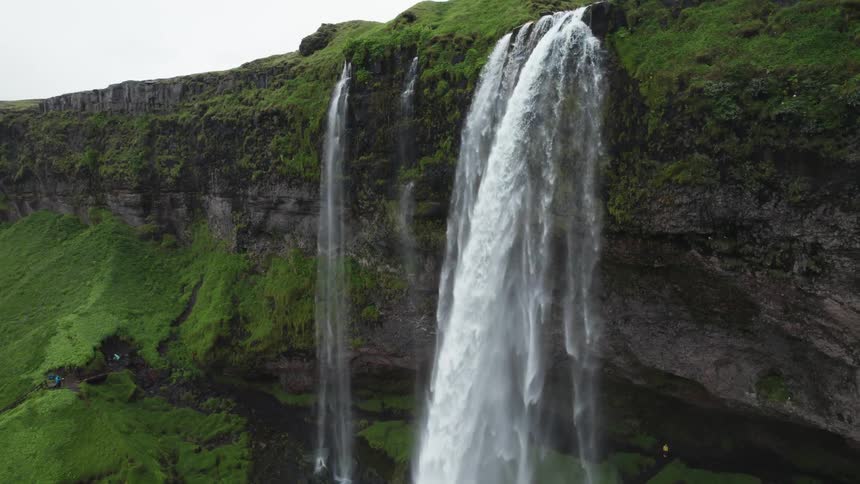 A waterfall pours from a cliff above a cavern on a cloudy day