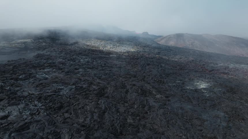 Aerial view of black dark volcanic terrain under the smoke near an active volcano caldera