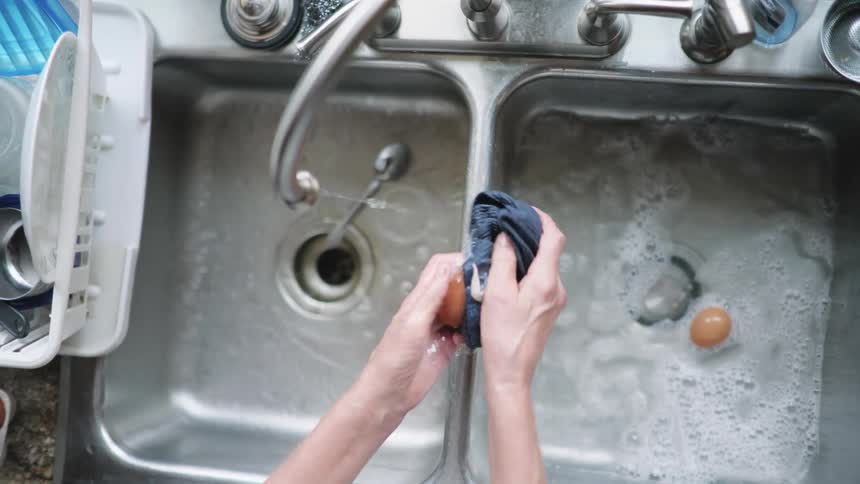 Overhead view of a hands washing eggs in a kitchen sink