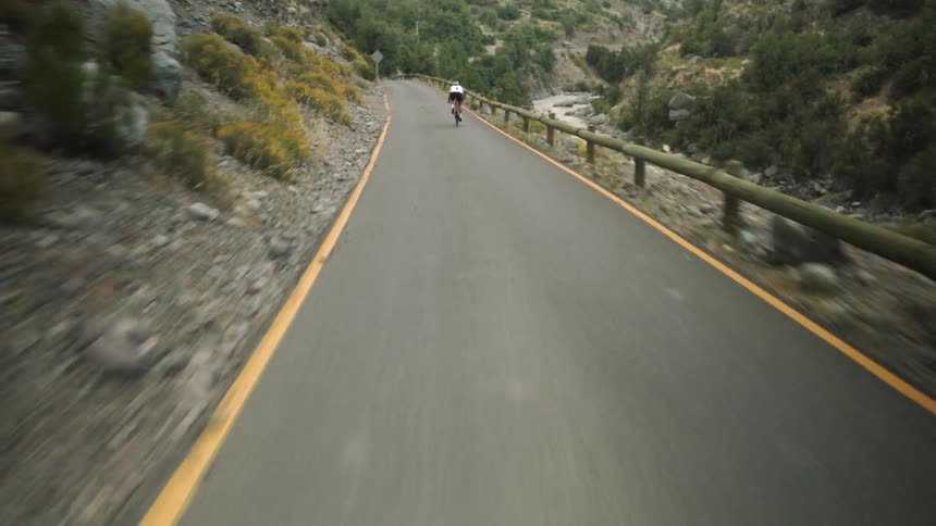 A bicyclist riding along some mountains near a river