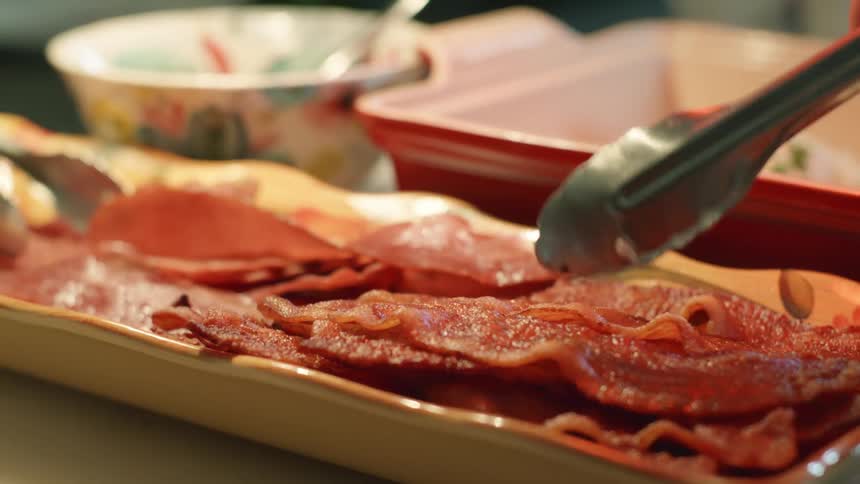 Person serving strips of hot crispy bacon using a pair of metal tongs