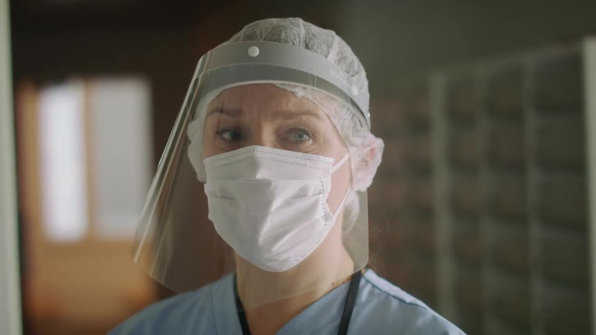 A doctor or nurse wearing a face mask and shield is staring off in a hospital