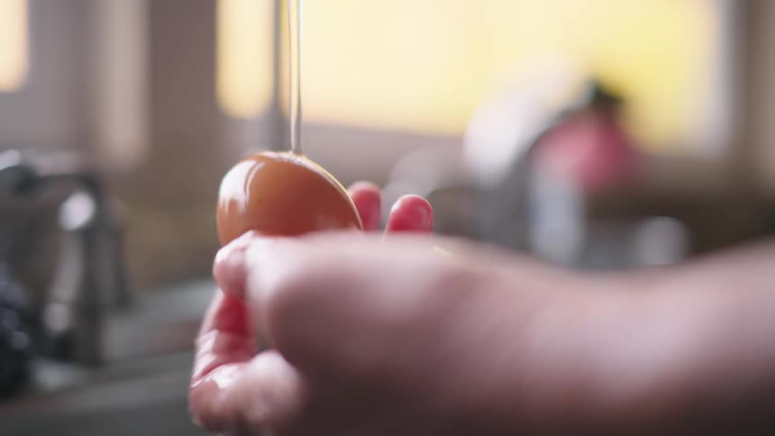 Woman cleaning a fresh egg under a stream of water from the kitchen sink at home