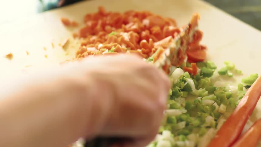 Woman finely chopping carrots, celery and onions on a cutting board as she prepares a meal