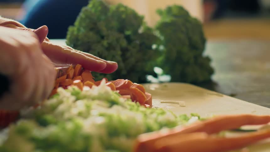 Someone is holding a knife and cutting vegetables on a cutting board