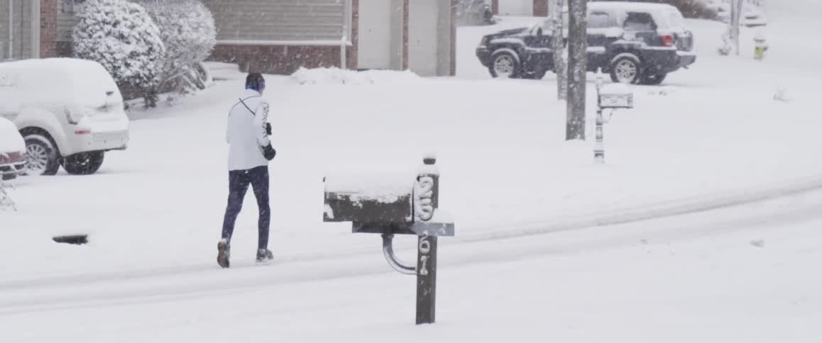 Someone jogs in the snow down the suburban street
