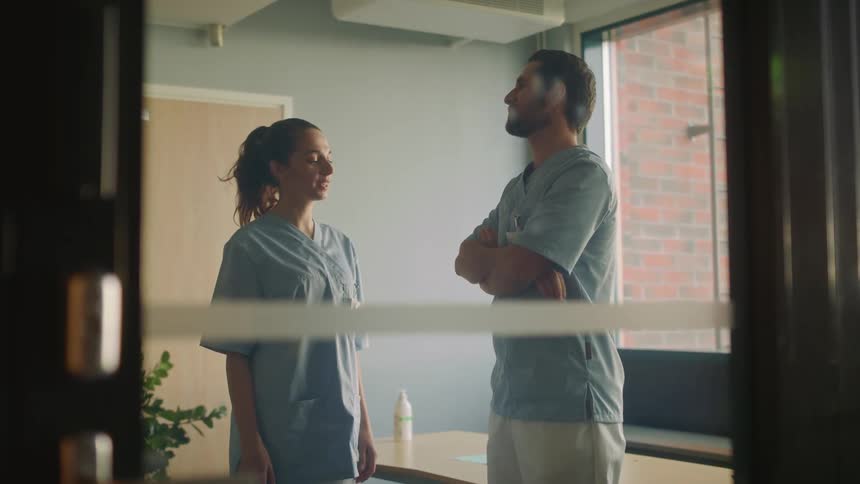 Two hospital workers are standing in a room talking and laughing