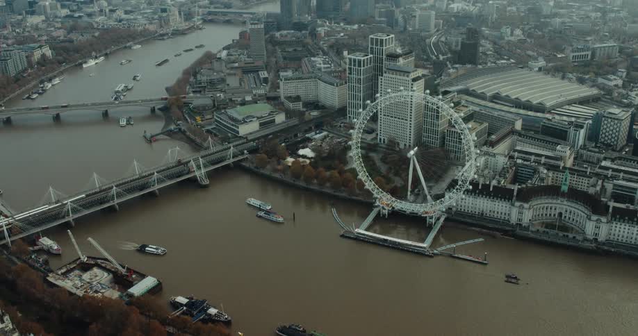 Boats move down river cutting through city past bridges and a ferris wheel