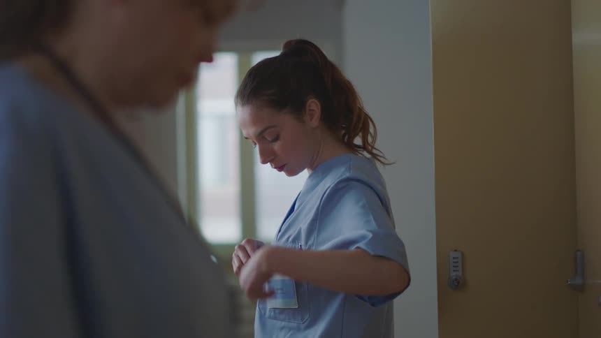 Female nurse with ponytail and scrub attaches id card to herself in clinic