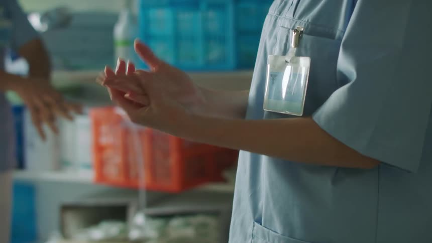 Two medical professionals in scrubs cleaning their hands with hand sanitizer