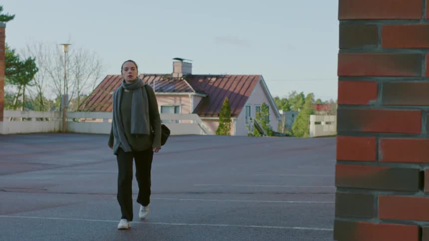 A young woman quickly walks down a street and turns a corner at a brick building