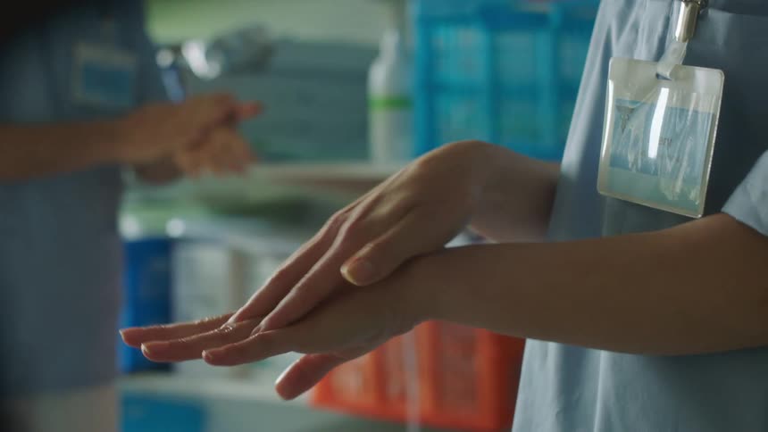 Medical personnel wearing scrubs sanitizes their hands