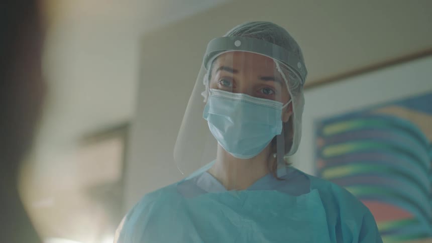 A doctor wearing protective gear waves goodbye to a patient