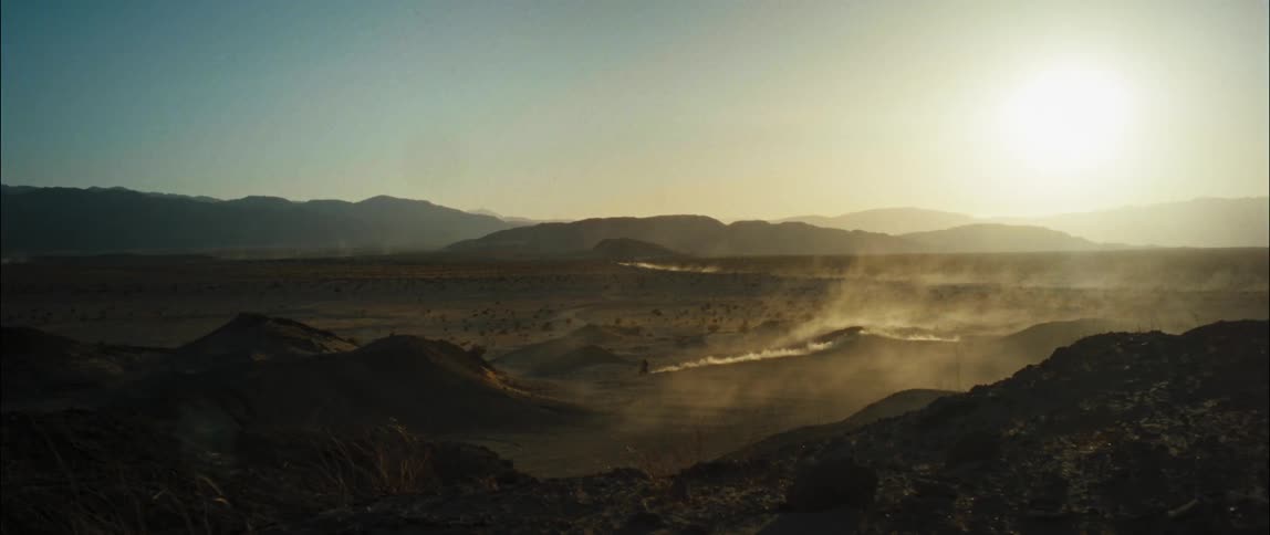 A motorcyclist rides offroad through an arid countryside during the day