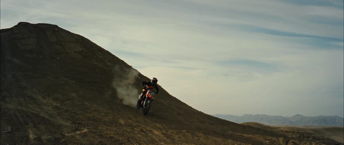 Motorcyclist races motorcycle down hill leaving a trail of dust