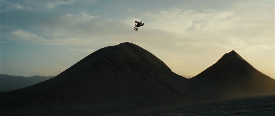 A dirt bike rider flies through the air while leaping across sand dunes