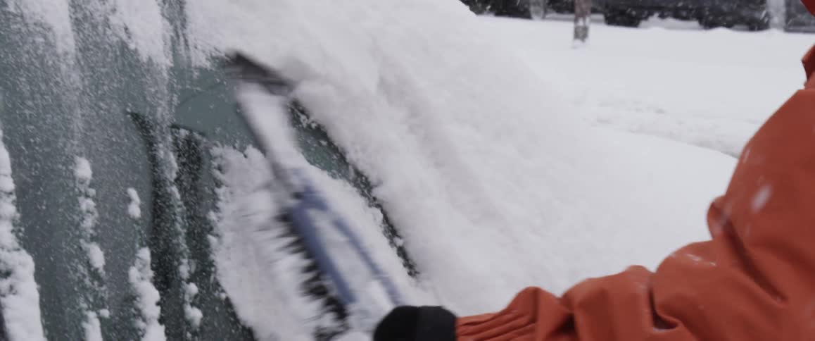 A person brushing snow off of a car