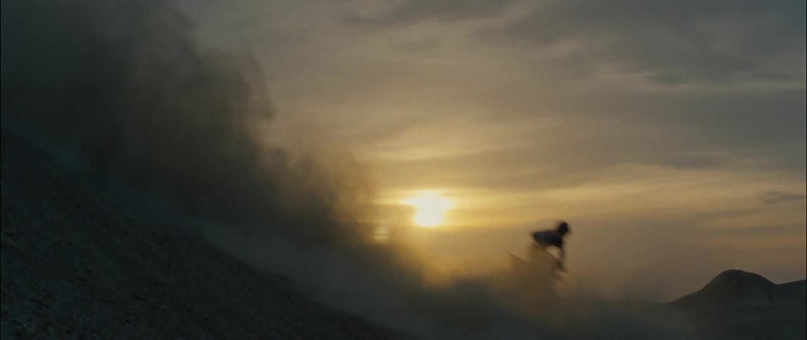 A dirt bike rider kicks up sand while riding up the side of a dune