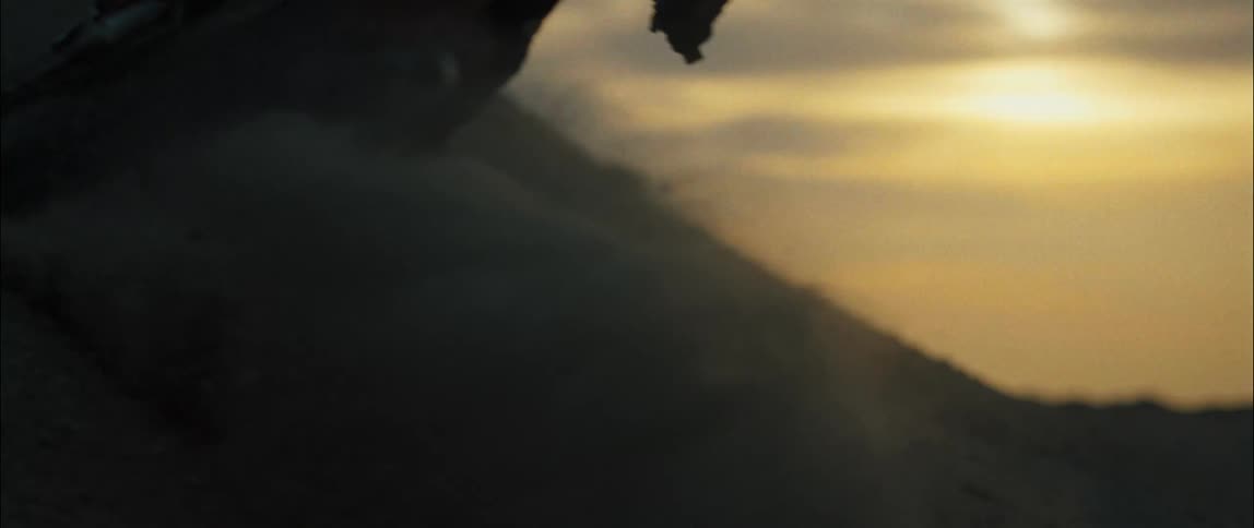 Dust flies as a person drives a motorcycle up a dirt hill